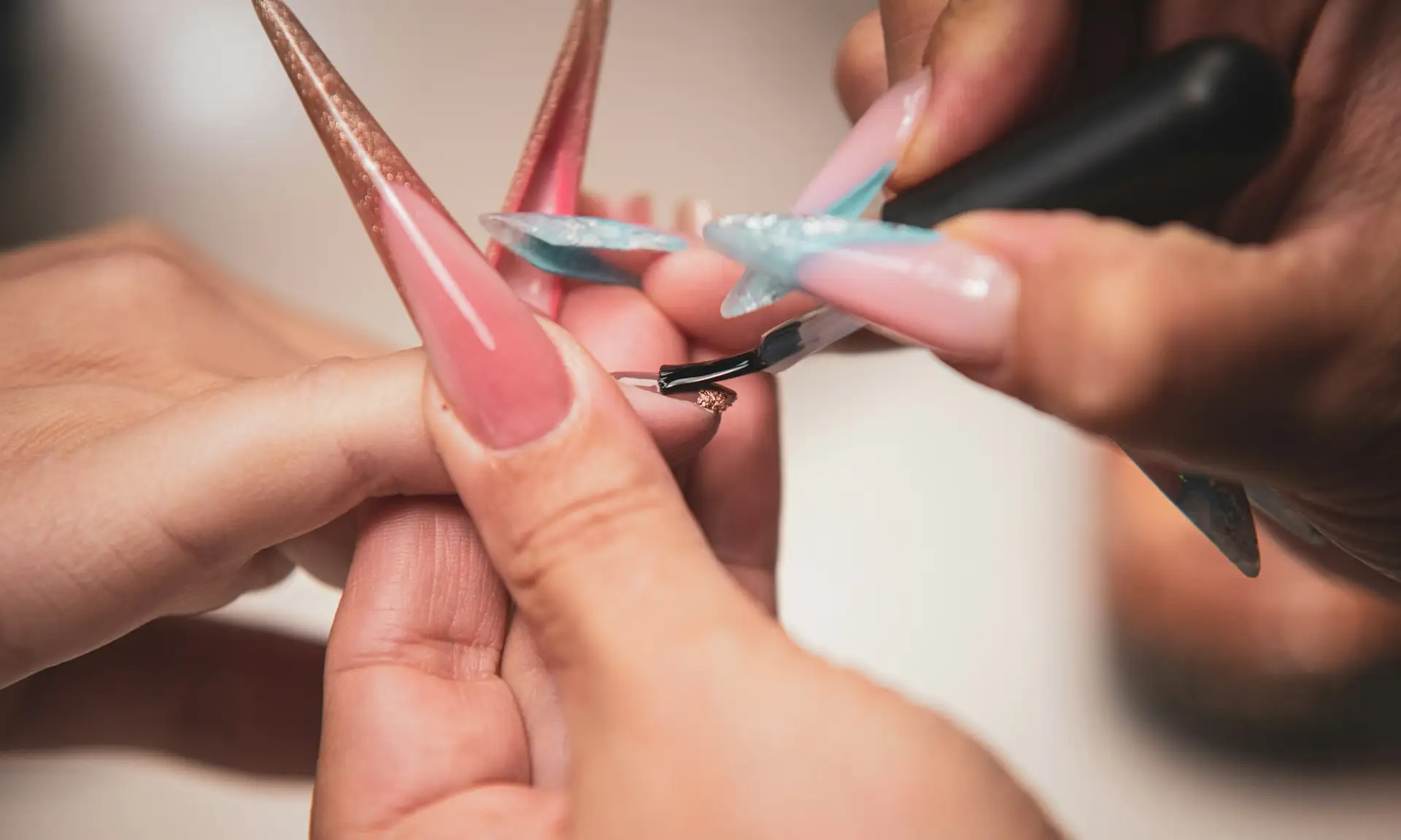 Long pink acrylic nail extensions being painted Beauty by Ana St Albans